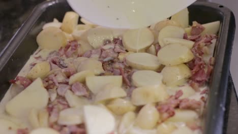 young woman pouring sauce over potato and bacon dish