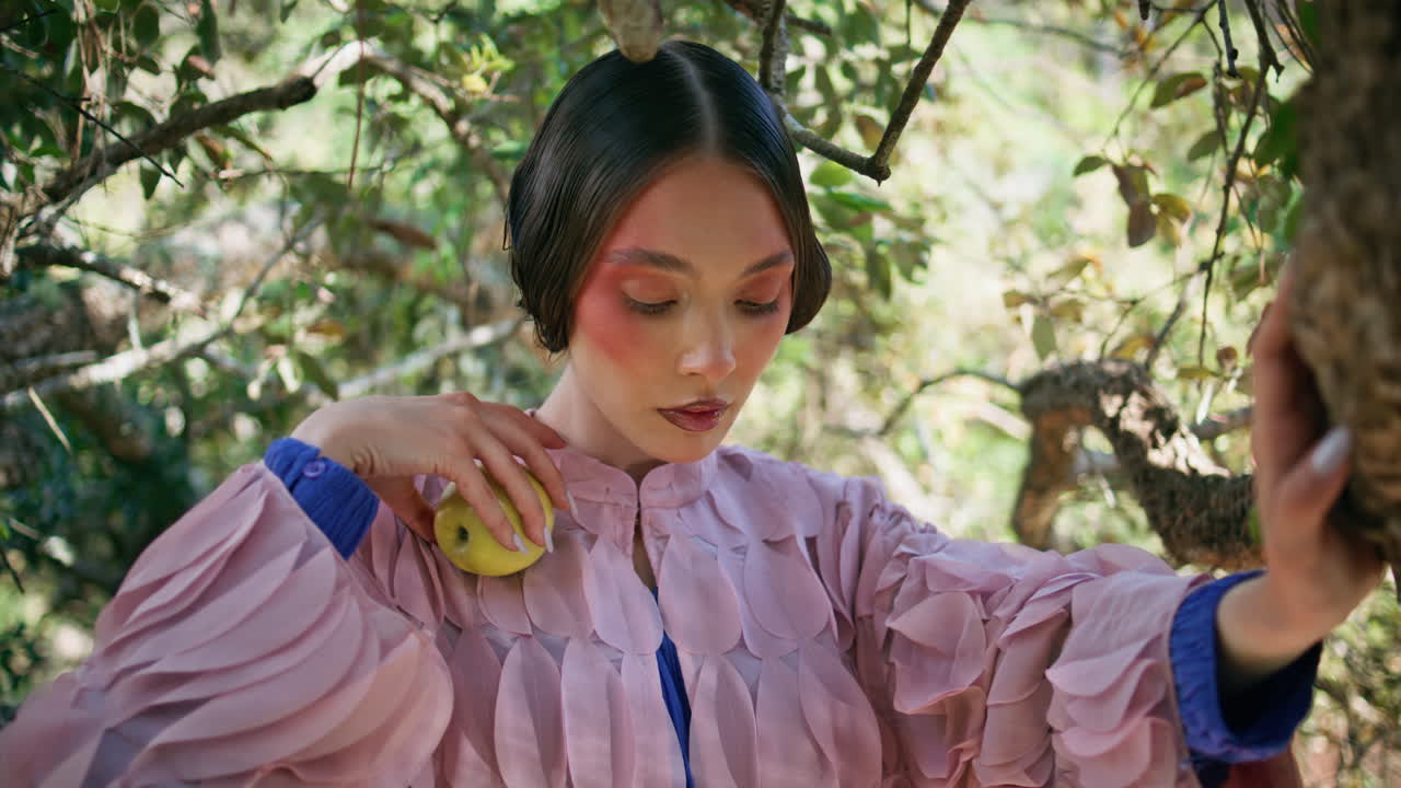 마법의 소녀는 나무에 서서 녹색을 바라보며 카메라를 쳐다보며 매혹적인 시선을 니다.