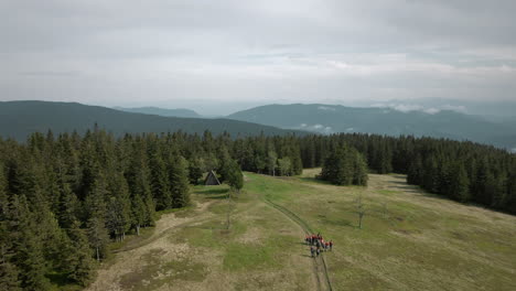 Drone-pan-shot-of-a-spruce-forest-and-a-group-of-young-scouts-walking-towards-the-cottage-near-the-forest