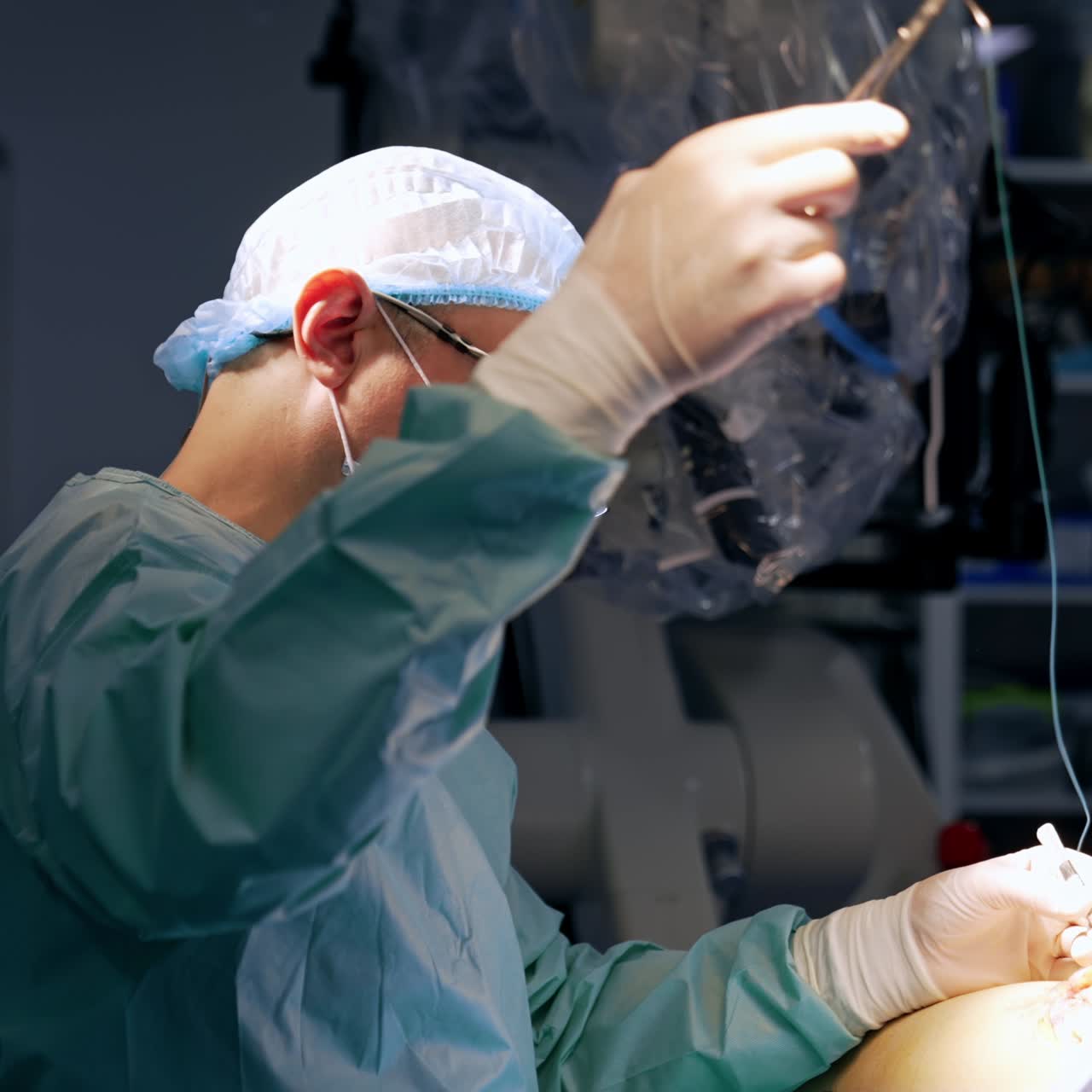 Male surgeon sitting at the patient applies metal tool and thread at operation. Doctor ending the surgery sewing the incision