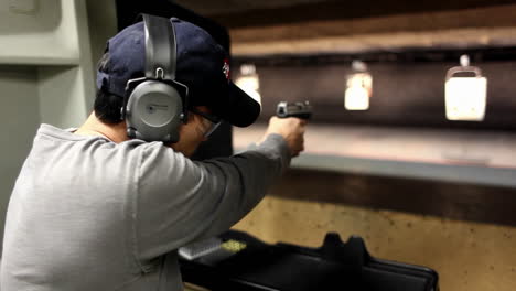 a man looks at the camera and then fires a hand gun at a target at an indoor shooting range