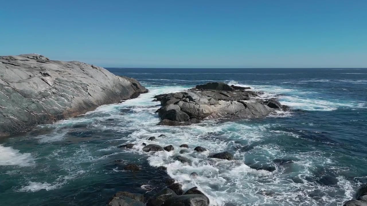 Voo rasante entre formações rochosas dramáticas de granito com ondas turquesa espumantes avançando por canais rochosos sob céu azul claro