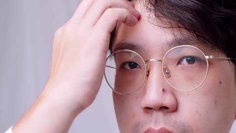 Close-up-Asian-man-with-glasses-and-healthy-good-hair-looking-to-the-camera-and-spoiling-himself-by-tidying-his-hair