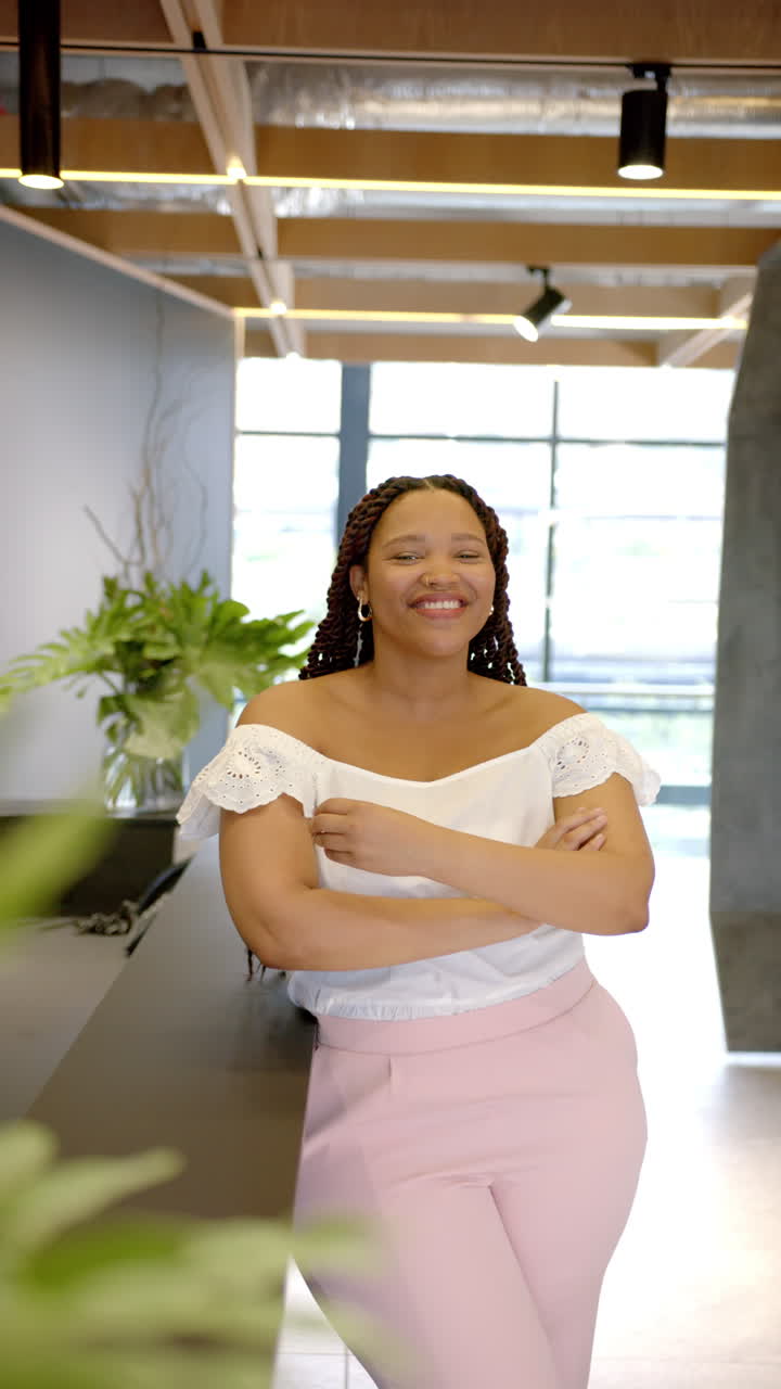 Vertical video: Leaning on counter in modern office, smiling woman wearing white blouse and pink pan