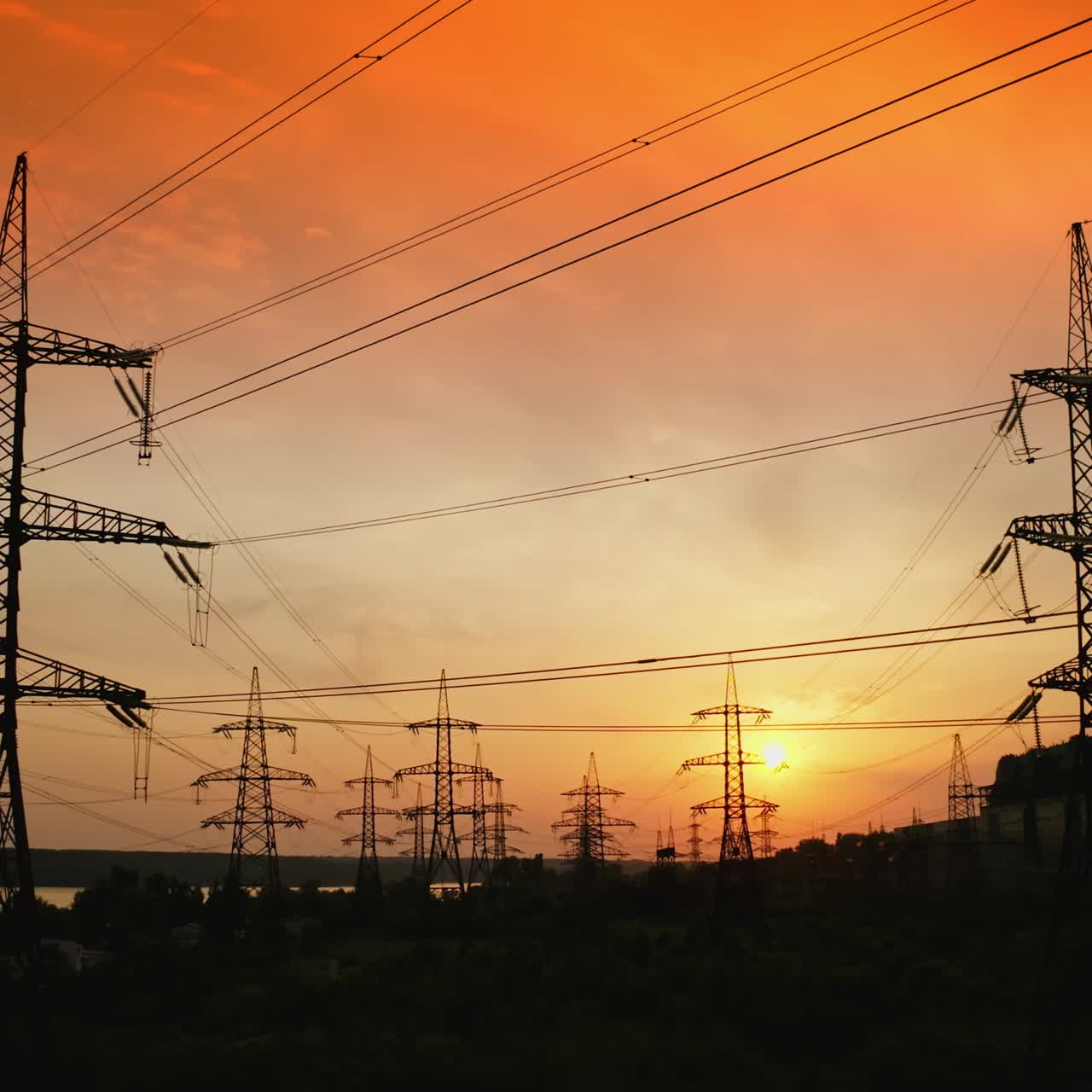 Electric towers against orange sky at sunset. High-voltage electricity pylons in the evening. Panoramic view of transmission lines. Camera rising