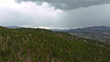 Aerial-drone-ascends-above-evergreen-trees-densely-packed-along-mountain-and-in-valleys