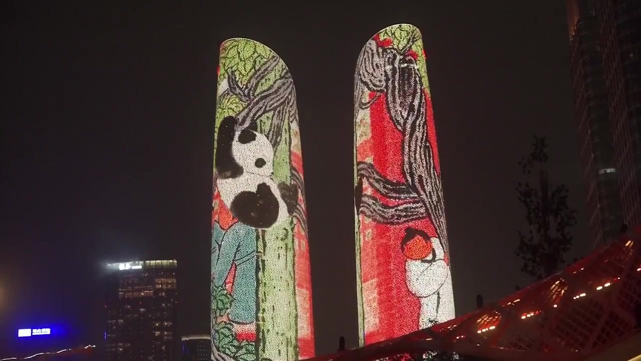Gece Finans Şehri İkiz Kuleleri'nin geniş, sabit bir çekimi, yeşil bambu ormanları arasında dinlenen ve tırmanan dev pandaların animasyonlu bir ışık gösterisini sergiliyor.