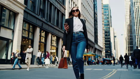 stylish woman walking through city street with phone