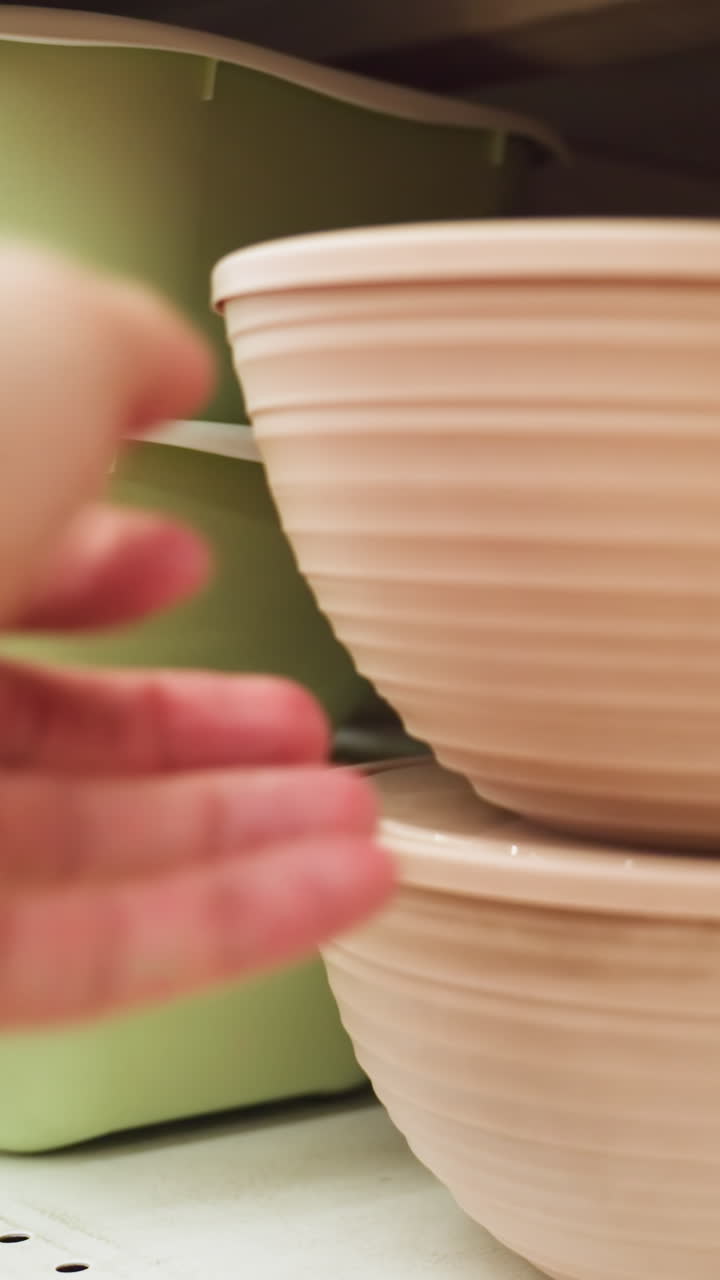view of a hand placing a bowl in the bowl section of a store. The scene features various bowls, including green and brown ones, neatly arranged on shelves