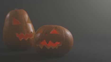 Smoke-effect-over-two-scary-face-carved-halloween-pumpkin-against-grey-background