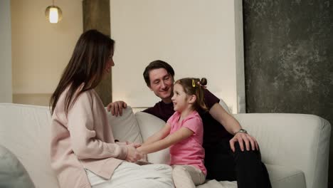young family with small daughter sitting on sofa talking and laughing together in the living room