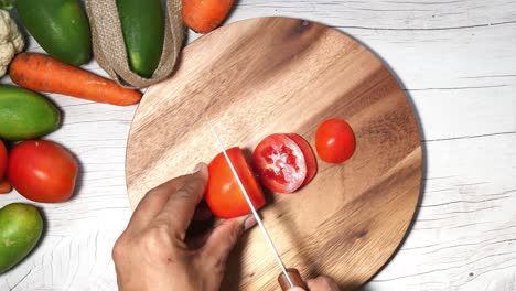 cutting a tomato on a wooden cutting board with vegetables