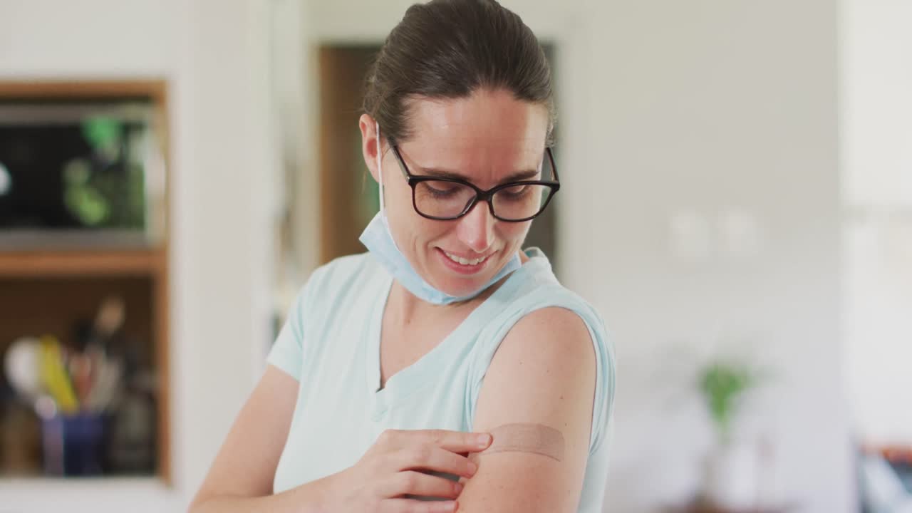 mujer caucásica con máscara facial apuntando a un vendaje en su brazo