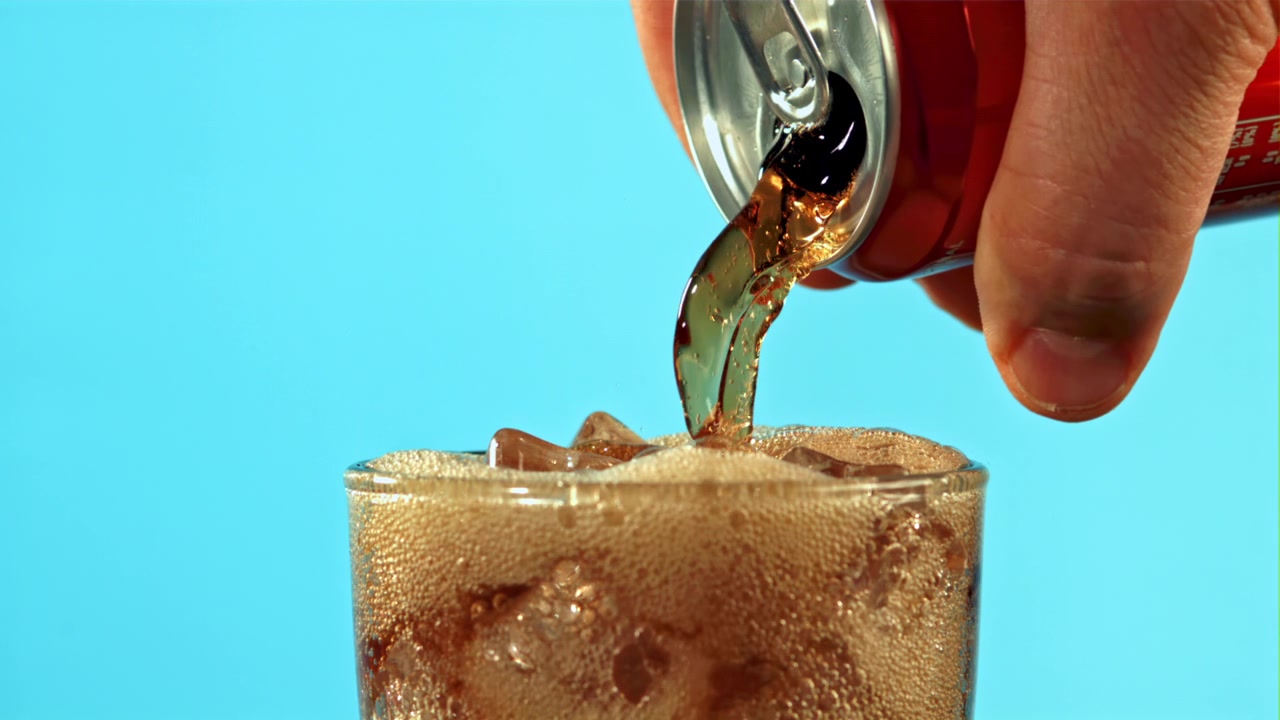 Versamento al rallentatore di bibita cola gassata in un bicchiere con ghiaccio