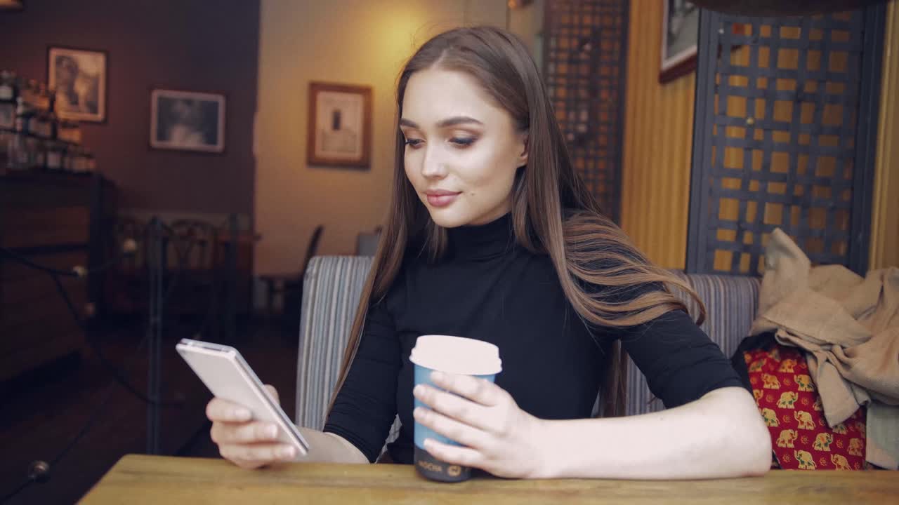 커피 한 잔을 들고 스마트폰을 사용하는 평상복 차림의 젊은 예쁜 여자