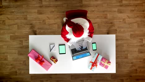 papá noel trabajando en la oficina en portátil, teléfono inteligente y tableta con chromakey, pantalla verde, escritura, vista aérea, disparo de arriba hacia abajo
