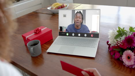 Caucasian-woman-holding-red-envelope-using-laptop-with-african-american-man-on-screen