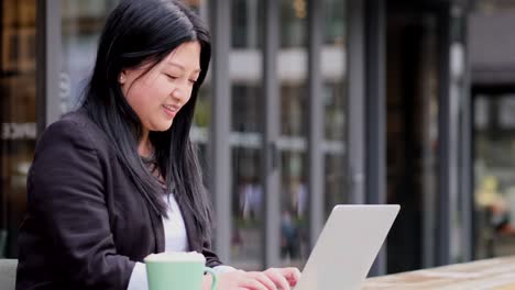 smiling asian young business woman working on laptop computer at outdoor cafe
