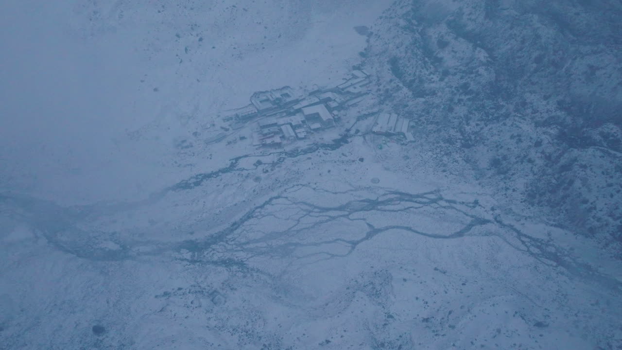Wide aerial drone shot of Lobuche village in Nepal’s Khumbu region on Everest Base Camp trek. Snowfall and irregular weather reveal high-altitude mountain housing in a heavenly, painting-like Himalaya
