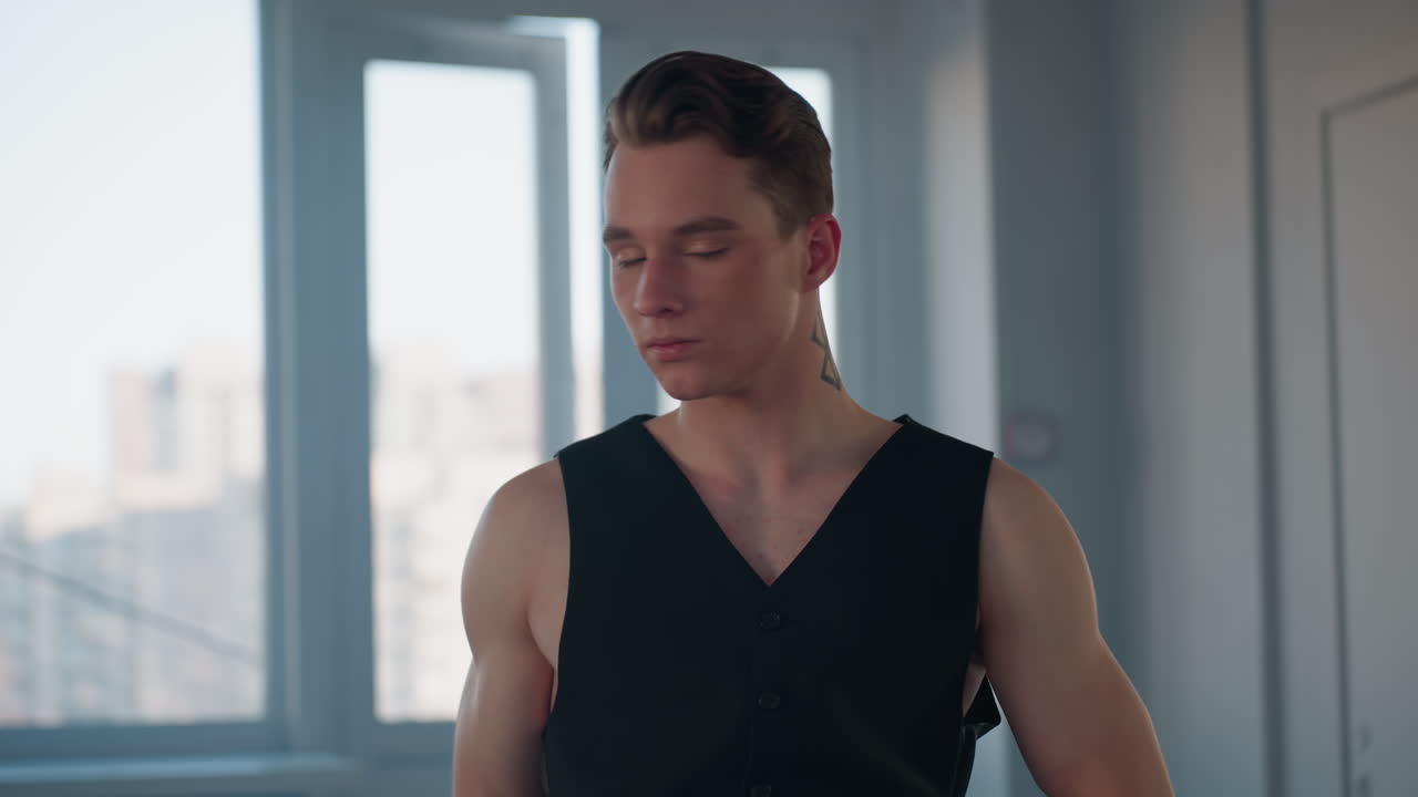 young man with tattooed neck stylishly removes fedora hat during dynamic dance pose by large studio window with soft natural light and subtle motion blur capturing expressive performance