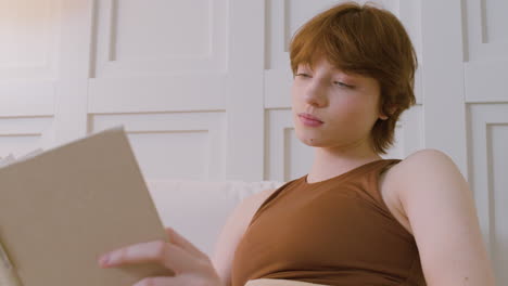vista inferior de la niña sentada en la cama leyendo un libro