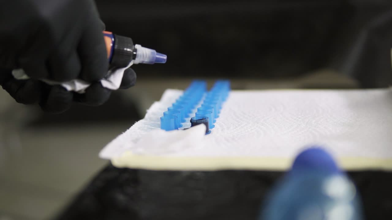 imágenes en primer plano del maestro del tatuaje dejando caer tinta azul en los contenedores. maestro del tatuaje profesional en guantes negros llenando las tazas con tinta para el proceso de trabajo. cámara lenta