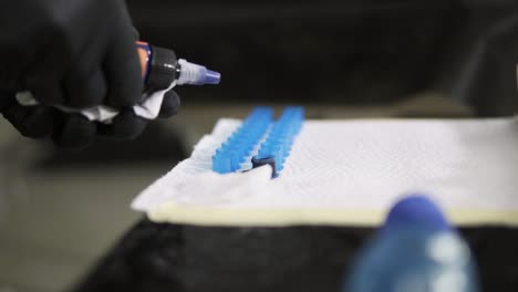 Close-up-footageof-tattoo-master-dropping-blue-ink-into-the-containers.-Professional-tattoo-master-in-black-gloves-filling-the-cups-with-ink-for-working-process.-Slow-motion