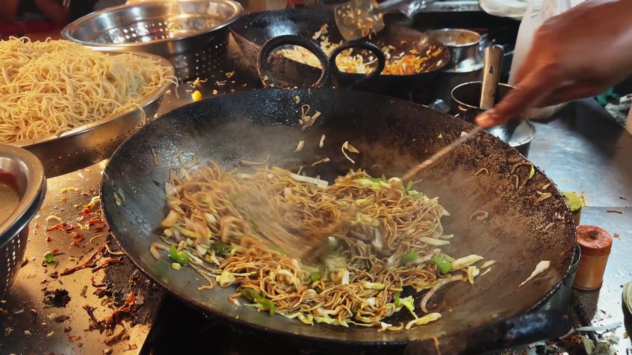Vista ravvicinata di noodles conditi e verdure colorate saltati a fuoco vivo in un wok tradizionale durante la frenetica preparazione di cibo da strada