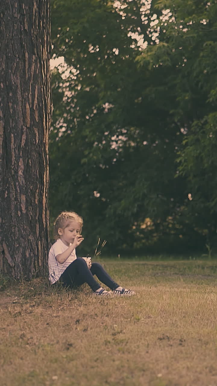 young lady with fair hair takes object from mouth sitting with yogurt container at huge brown tree trunk slow motion