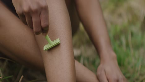 woman shaves legs outdoors on grass