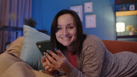 mujer acostada en el sofá en casa usando el teléfono móvil comunicándose en redes sociales o compras en línea