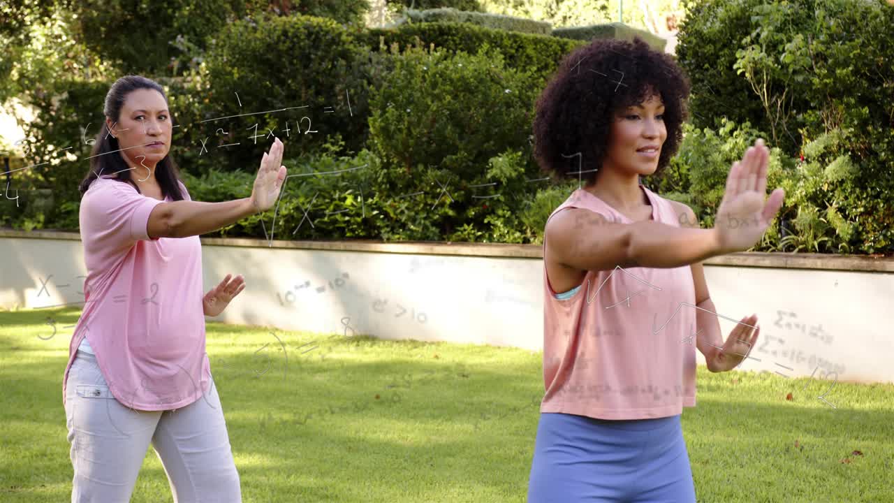 Lead woman initiating forward step, two women practicing slow tai chi on grassy lawn for fitness