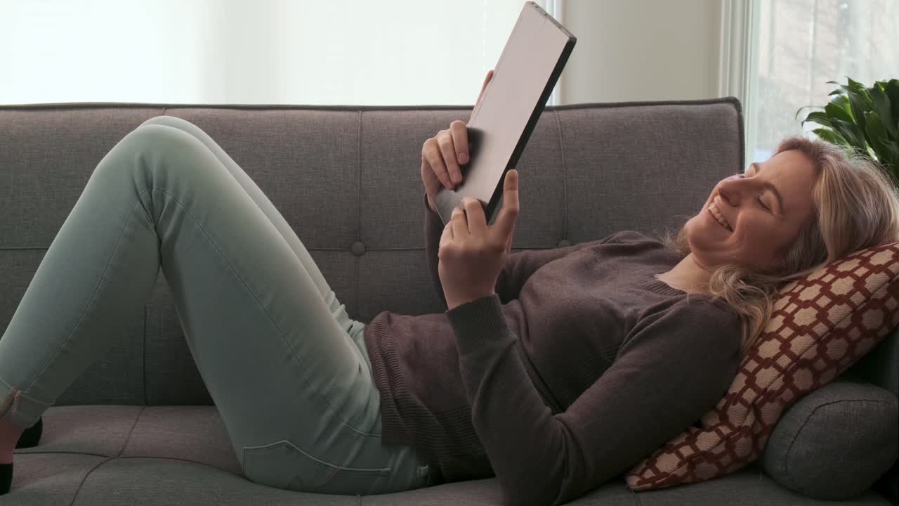 Attractive young blonde woman smiling at something on her tablet