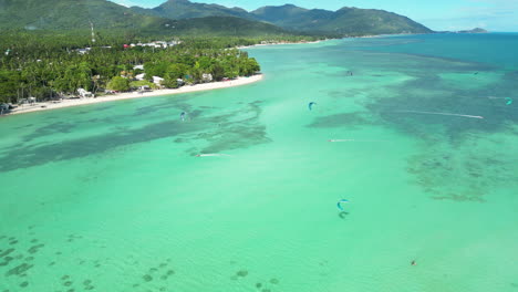 Aerial-over-the-turquoise-blue-waters-with-kite-surfers-on-Ko-Pha-Ngan-Island,-Thailand