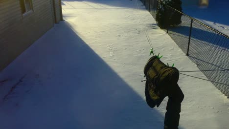 wide shot looking outside at the back yard as afternoon shadows fall on the snow, with wind blowing a black winter coat on a clothesline