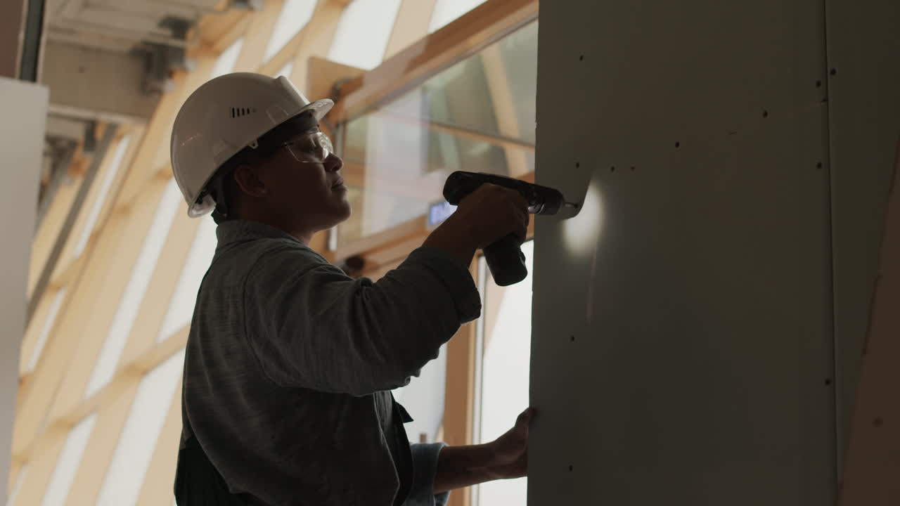 Worker Using Drill on Plasterboard Wall