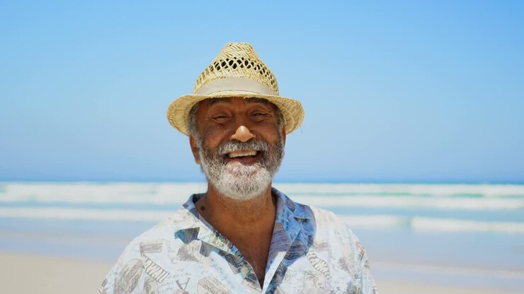 Front view of happy active senior African American man with hat standing on beach in the sunshine 4k