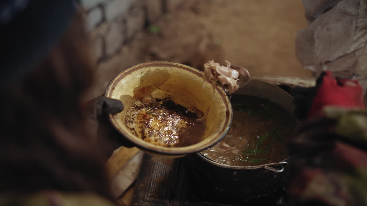 Survivor scoops food from metal pot into worn enamel bowl over flame inside brick shelter, using ladle with red glove, symbolizing hunger, struggle, and resilience in harsh post-apocalyptic condition