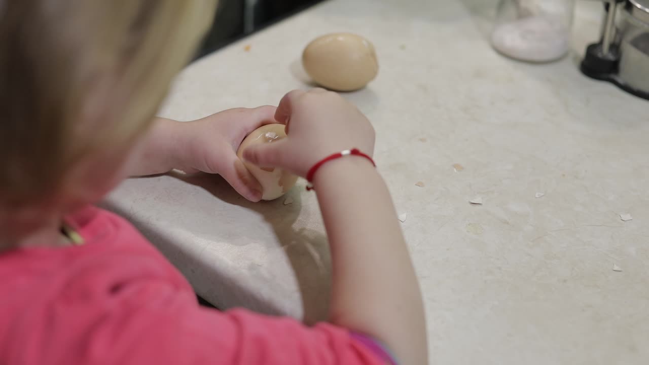 Nahaufnahme eines kleinen Mädchens, das die Schale von einem gekochten Hühnerei schält.