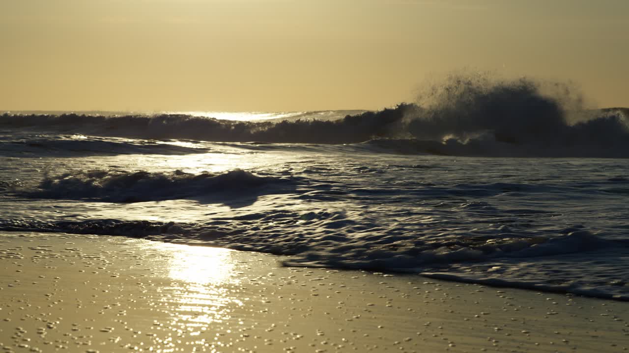 A shot captures waves racing across the beach, leaving glistening trails on the wet sand and creating a fine mist, as the sun paints the scene in a golden hue.