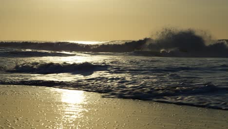 a shot captures waves racing across the beach, leaving glistening trails on the wet sand and creating a fine mist, as the sun paints the scene in a golden hue.