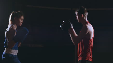 Female-boxer-punching-a-focus-mitts-with-boxing-gloves-in-a-smoky-gym