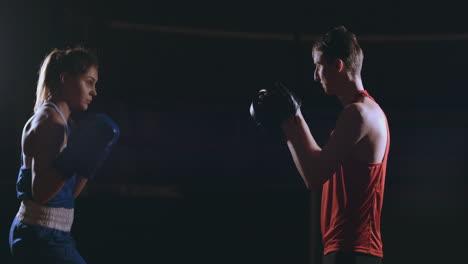 female boxer punching a focus mitts with boxing gloves in a smoky gym