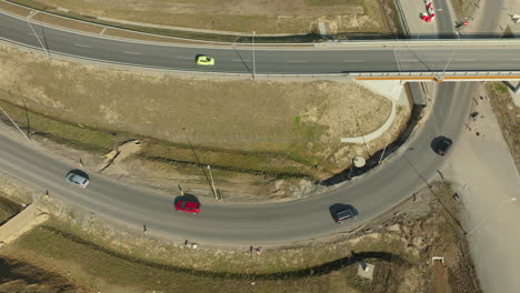 Looking-down-upon-a-curved-road-section,-cars-navigate-the-bend-against-a-backdrop-of-barren-land,-showcasing-the-flow-of-traffic-and-the-infrastructure's-integration-with-the-landscape