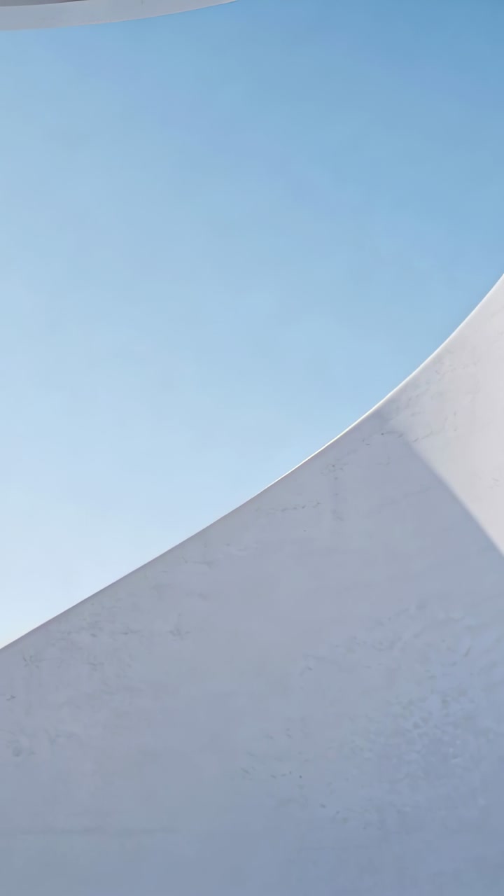 Vertical video: Camera framing curved white wall at outdoor plaza, revealing thin rim and shadow