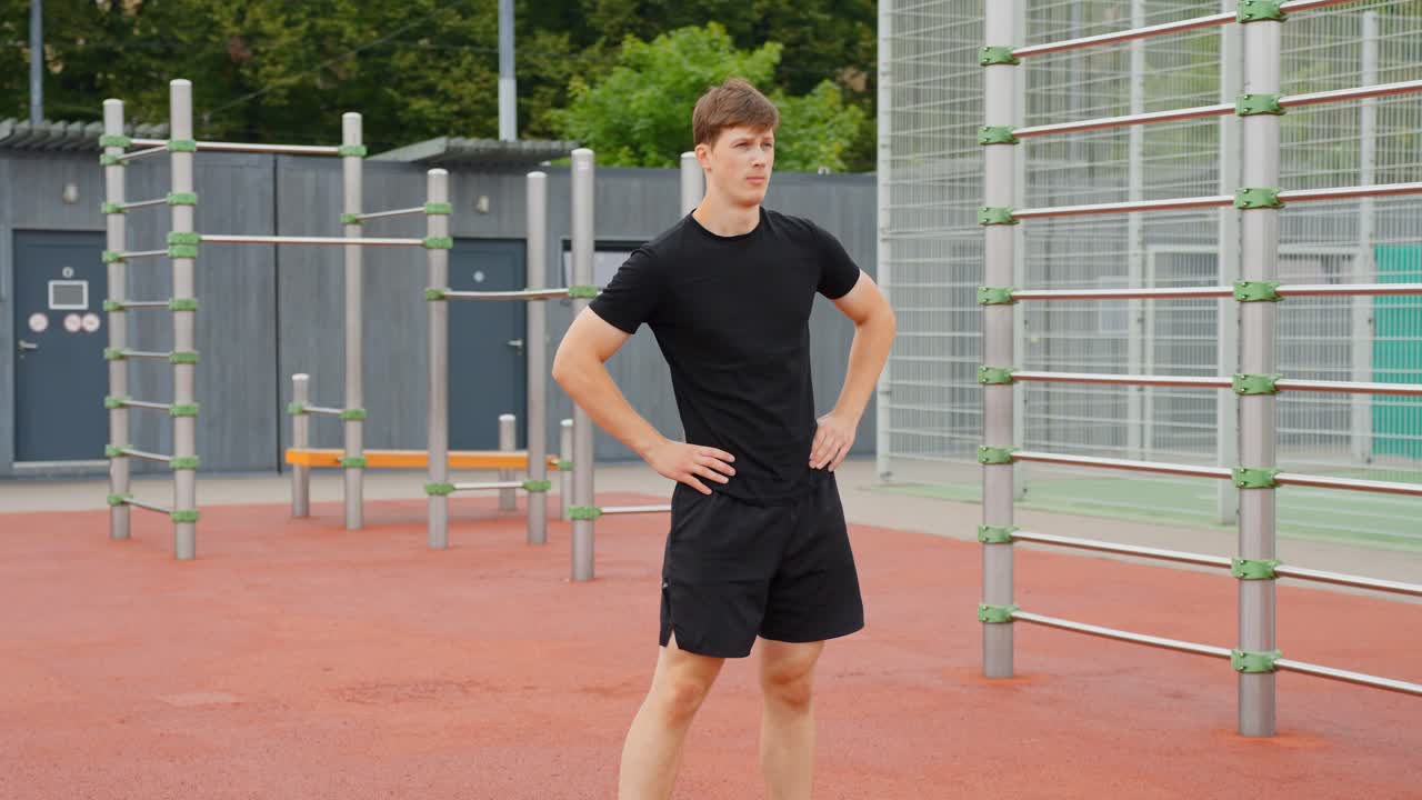 Fixed shot of a young man standing in an outdoor sports area, moving his hips in circular motions