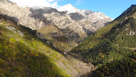 aérea: volando entre dos montañas con el valle debajo y montañas cubiertas de nieve al fondo