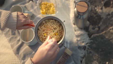 Top-down-slow-motion-footage-of-a-woman-cooking-noodles-mixed-with-corn-in-the-outdoors-at-golden-hour