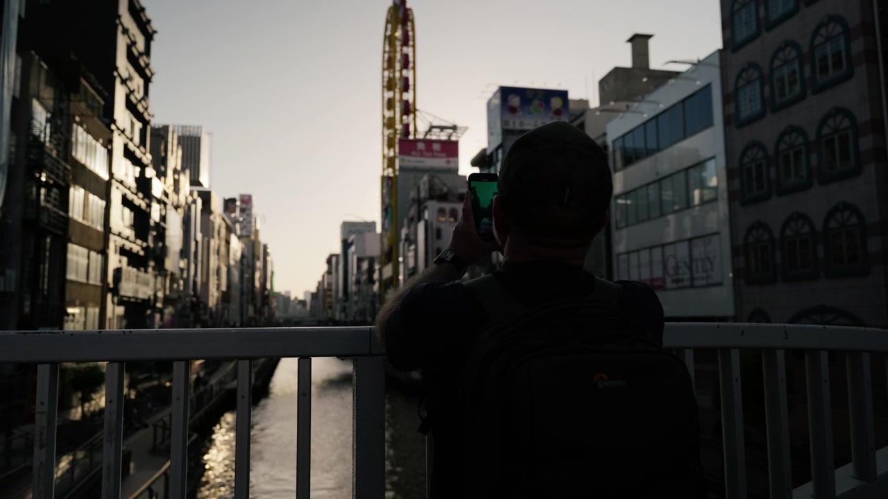 男性シルエット、写真を撮る観光客、スマートフォン、都市の建物。