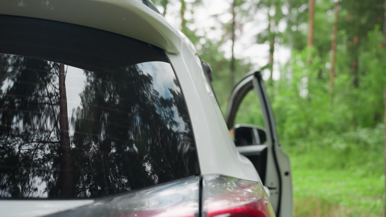 Back view of woman with long red hair entering white SUV surrounded by lush green forest, calm natural scenery reflecting peaceful travel mood, outdoor lifestyle and serene summer atmosphere
